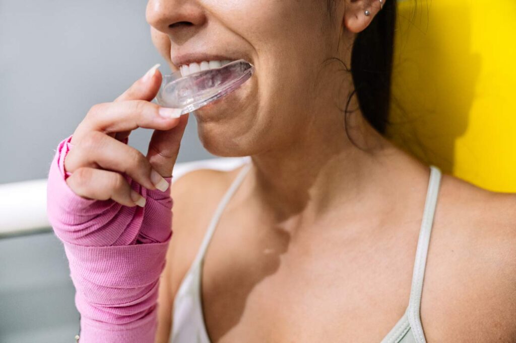 Atleta femenina colocándose un protector bucal durante un entrenamiento de boxeo en un ring