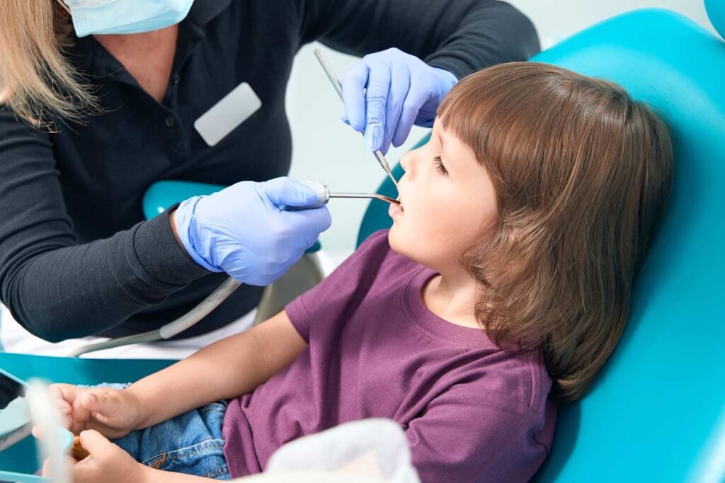 Dentista mascarilla y guantes examinando la boca de una niña pequeña utilizando herramientas dentales