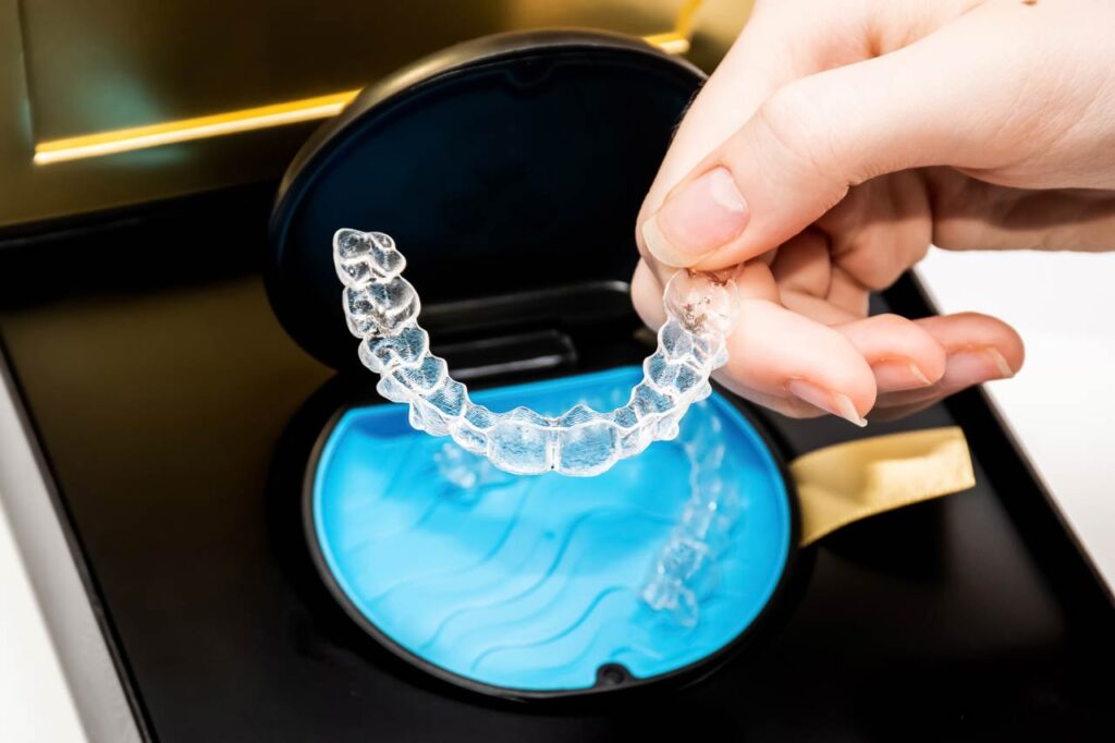 Mano de una mujer cogiendo unos alineadores transparentes en caja. Brackets invisibles. Enderezadores dentales transparentes. Brackets transparentes.